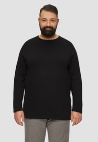 Zwarte longsleeve T-shirt met een ronde hals, gemaakt van textuurstof. Heeft een ontspannen pasvorm en rechte zoom, gedragen met grijze geblokte broek.