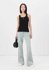 Svart utenermet tanktopp med en liten logo, kombinert med lyseblå populære jeans og hvite joggesko. Modellen holder en svart veske.