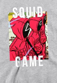 Red hoodie graphic featuring two figures with masks, set against a colorful background. Text reads "SQUID GAME" in bold white letters.