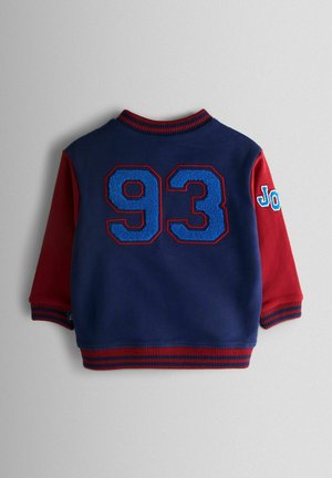 Mørkeblå sweatshirt med røde ærmer. Har stort, blåt tekstureret "93" på ryggen samt røde og blå stribede manchetter og krave.