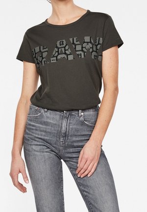 Donkergroene katoenen T-shirt met korte mouwen, met een grote grafische tekst "RAW" in zwart en grijze patronen over de voorkant.