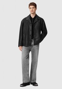 Zwarte leren jas met knoopsluiting, met inkeping kraag en twee zijzakken, gecombineerd met grijze wijde jeans en zwarte schoenen.