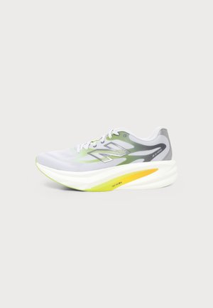 Hellgrauer und weißer Laufschuh mit neongrünen und gelben Akzenten und dicker, gepolsterter Sohle, von der Seite auf einfachem Hintergrund gesehen.