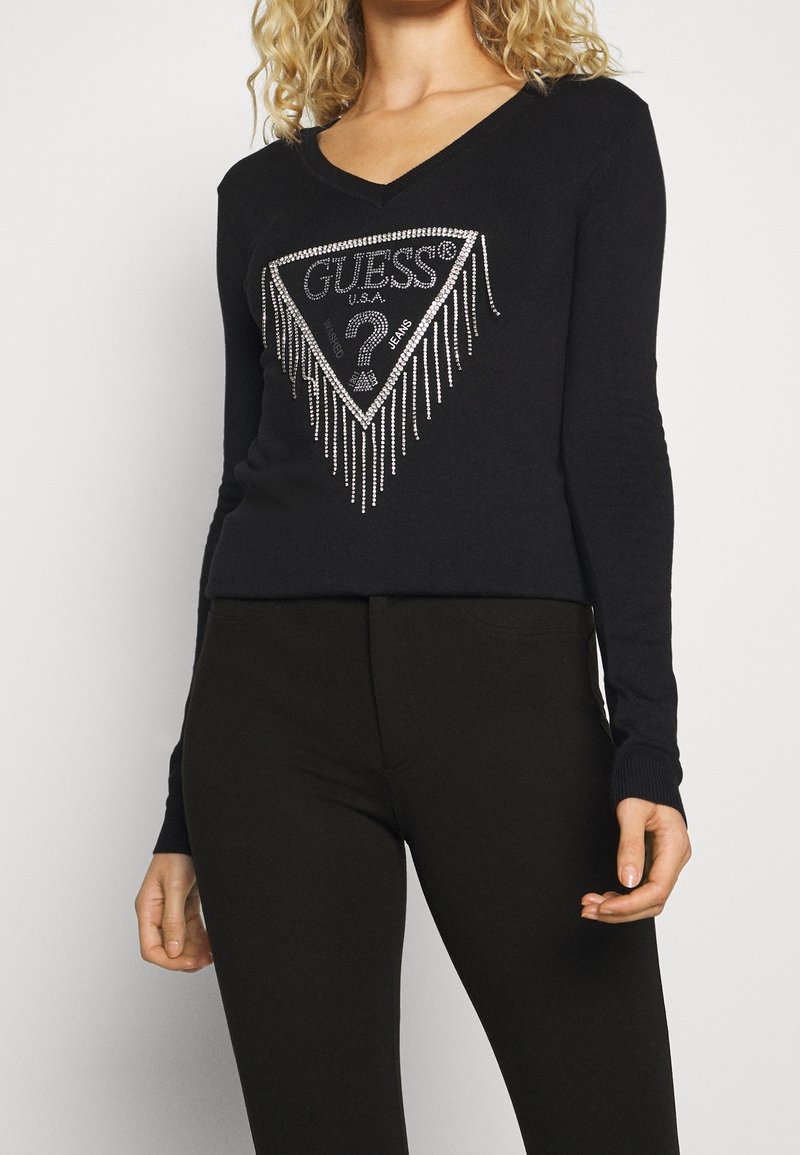 Musta pitkähihainen paita V-kaula-aukolla, jossa edessä kolmionmuotoinen logo, jossa on strassikoristeita. Pehmeä pinta ja vartalonmyötäinen malli.