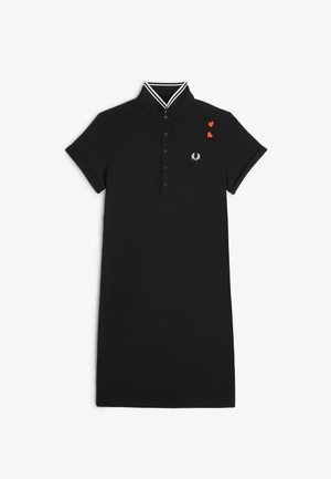 Abito polo nero a maniche corte con colletto a righe bianche, bottoni a forma di cuore, logo alloro bianco sul petto e due piccole toppe a forma di cuore rosso.