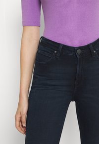 Bodysuit de rayas moradas y jeans ajustados azul oscuro, con cintura alta, cinco bolsillos y cierre estándar de botón y cremallera.