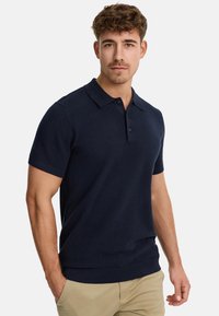Polo shirt bleu marine à manches courtes avec un col classique, un tissu texturé et une coupe ajustée. Les boutons sont visibles au niveau du col.