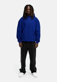 Blauer Kapuzenpullover aus Baumwolle mit Kängurutasche, kombiniert mit schwarzen weit geschnittenen Hosen und weißen Sneakers.