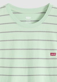 T-shirt Levi's vert clair avec fines rayures horizontales foncées et col rond, avec un petit patch logo rouge Levi's sur la poitrine.
