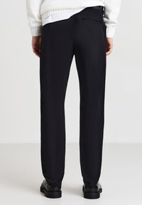 Pantaloni neri in tessuto liscio con una vestibilità comoda. Caratterizzati da una tasca sul retro, scendono dritti fino alla caviglia e sono abbinati a scarpe nere.