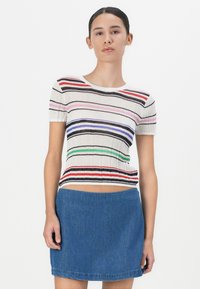 Gestreiftes kurzärmliges Oberteil mit gerippter Textur, das horizontale Linien in Rot, Pink, Blau und Grün auf einem cremefarbenen Hintergrund aufweist, kombiniert mit einem Jeansrock.