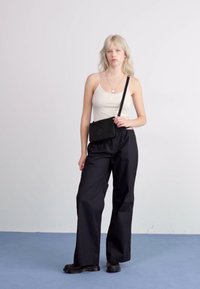 Sorte brede bukser med løs pasform, parret med en hvid tanktop og en lille sort crossbody taske. Glat tekstur, minimalistisk design.
