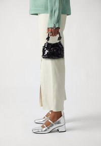 Borsa a tracolla nera con paillettes e manico rotondo; abbinata a scarpe Mary Jane argentate e una giacca verde menta chiaro sopra pantaloni bianco sporco con spacco laterale.