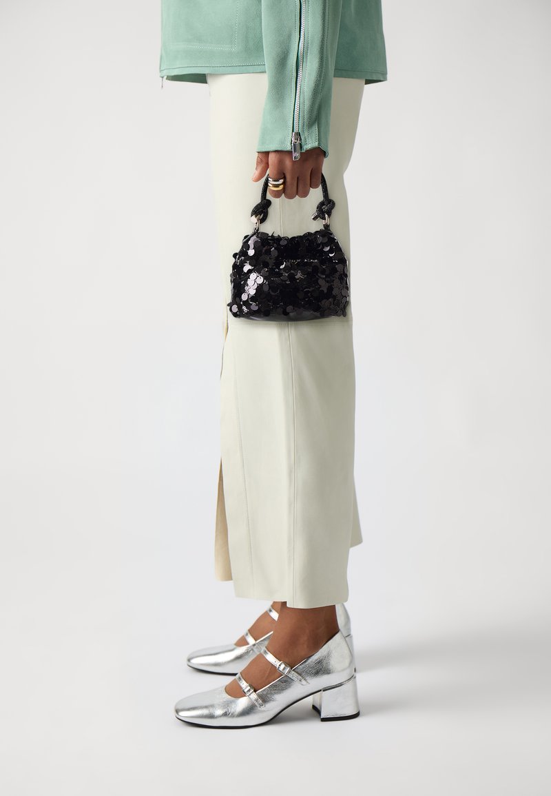 Borsa a tracolla nera con paillettes e manico rotondo; abbinata a scarpe Mary Jane argentate e una giacca verde menta chiaro sopra pantaloni bianco sporco con spacco laterale.