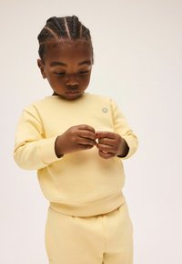 Sudadera de algodón amarilla y pantalones a juego con puños acanalados, con un pequeño logo de carita sonriente en el pecho, textura lisa.