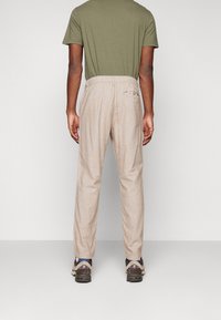 Light beige tapered trousers with a textured fabric, elastic waistband, and a back pocket, paired with a green shirt and brown footwear.