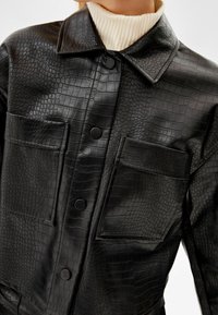 Czarna kurtka z imitacji skóry o fakturze krokodyla, z kołnierzem, dwoma przednimi kieszeniami i zapięciem na guziki.