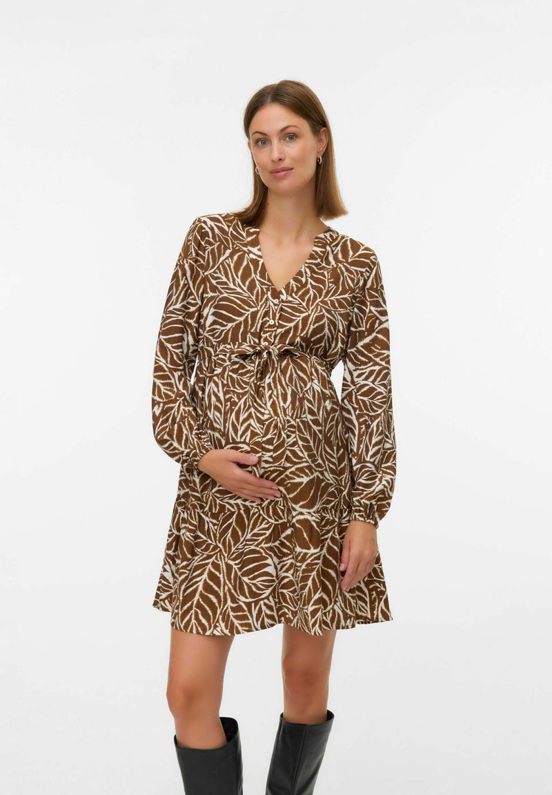 Robe de maternité à motif de feuilles marron avec des manches longues, un décolleté en V, une taille cintrée et un ourlet évasé, associée à des bottes noires montantes.