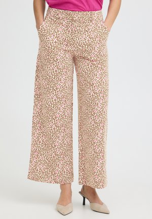 Femme portant un pantalon à jambes larges avec un imprimé léopard beige et rose et des chaussures slingback beiges à talons, mains dans les poches.
