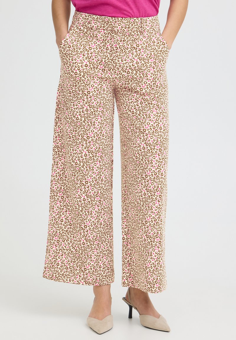 Femme portant un pantalon à jambes larges avec un imprimé léopard beige et rose et des chaussures slingback beiges à talons, mains dans les poches.