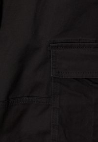 Zwarte katoenstof met een vlakke zakdetail en contrasterende stiksels. De textuur lijkt glad en duurzaam, geschikt voor casual kleding.