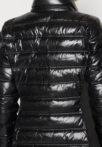 Sort pufferjakke med en blank finish, vandret quiltet design, lynlåselementer og en høj krave. Materialet fremstår glat og holdbart.