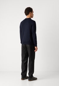 Navy knit sweater with round neck, long sleeves, and ribbed cuffs, paired with dark textured trousers and black sneakers.