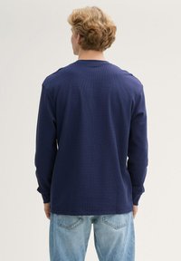 Marineblaues Langarmshirt mit strukturierter Webart, Rundhalsausschnitt und eng anliegenden Ärmeln. Der Stoff wirkt weich und leicht. Lockerer Schnitt.