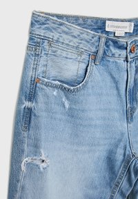 Jeans de mezclilla azul claro con acentos desgastados, que cuentan con una cintura alta, cinco bolsillos y herrajes metálicos en tono cobre. Etiqueta de la marca visible.