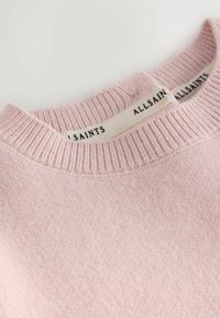 Svetlo ružový pletený sveter s rebrovaným výstrihom a mäkkou textúrou, s nášivkou s nápisom "ALLSAINTS" na vnútornej strane.