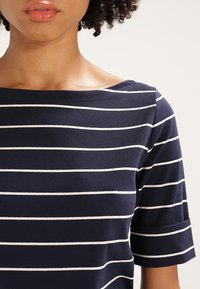 Mörkblå kortärmad topp med vita horisontella ränder, med en bred båthalsringning och mjukt bomullstyg.