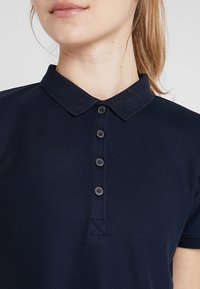Navy blue polo shirt with a textured fabric, featuring a collared neckline and front placket with five black buttons.