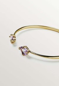 Brazalete de oro con dos piedras preciosas moradas de corte facetado, sujetas en engastes metálicos con pequeñas piedras de acento al lado de cada gema.