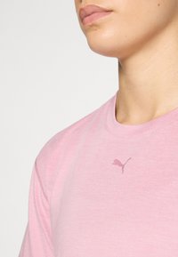 Rožinė medvilninė marškinėliai su apvalia iškirpte, trumpomis rankovėmis ir subtiliu Puma logotipu, šiek tiek tamsesnės rožinės spalvos, ant krūtinės.