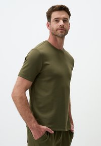 T-shirt verde oliva a maniche corte realizzato in un morbido tessuto elasticizzato, con scollatura rotonda e silhouette aderente, senza pattern visibili.