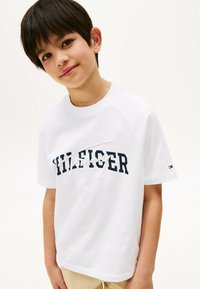 Hvid T-shirt med korte ærmer, prydet med et marineblåt "HILFIGER" logo med hvide detaljer. Den er lavet af bomuld, har en rund halsudskæring og en afslappet pasform.