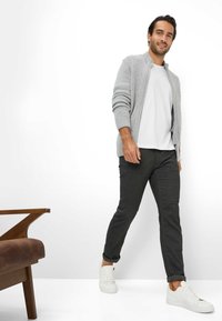 Lys grå cardigan med ribbede ærmer, hvid t-shirt, mørkegrå bukser og hvide sneakers; trækstol i forgrunden. Simpelt moderne stil.