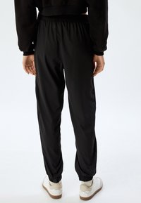 Zwarte sportbroek met een elastische tailleband, aansluitende boorden en een gladde, lichte stof. Gekocht met witte sneakers.