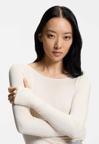 Long-sleeve, form-fitting, light beige top with a scoop neckline and textured fabric. Sleeves extend past the wrist for added coverage.