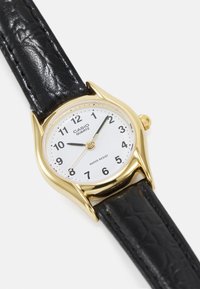Montre à quartz dorée avec un cadran blanc, bracelet en cuir noir, index clairs et fonction étanche.