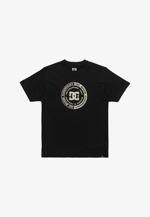 Black cotton t-shirt featuring a circular DC logo in gold, with text detailing brand name and year established. Short sleeves and crew neck.