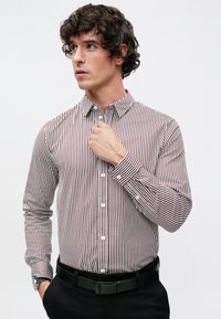 Camisa de botones con rayas verticales estrechas en rojo y blanco, cuello clásico, mangas largas y puños redondeados tipo barril. Con un ajuste entallado.