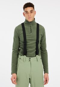 Pull en polaire vert foncé avec col haut et fermeture éclair à l'avant, complété par un pantalon vert clair avec bretelles noires et fermeture à bouton.