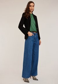 Musta bleiseri, vihreä teksturoitu paita, leveät siniset farkut ja käärmeennahkakuosiset korkokengät. Asusteessa on muotoiltu siluetti ja vastakkaisia värejä.