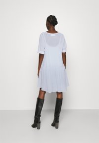 Světlé modré šaty s kratkým rukávem a rozšířeným lemem, zdobené nařasenými detaily, vyrobené z texturované tkaniny. Slučují se s černými kozačkami na podpatku do výšky kolen.