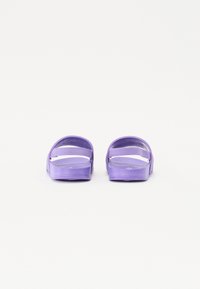 Lilla sklidesandaler med en glatt, blank tekstur og brede stropper. Åpen tå-design med flat såle. Enkel og minimalistisk konstruksjon.