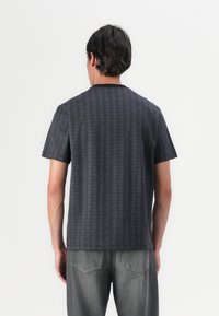 Cămașă cu mânecă scurtă de culoare gri închis, cu un model geometric, guler rotund și țesătură netedă. Asortată cu blugi din denim gri deschis.