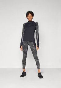 Μαύρο αθλητικό τοπ με μισό φερμουάρ, συνδυασμένο με μαύρο και γκρι κολάν με σχέδια. Και τα δύο έχουν μακριά μανίκια και ανακλαστικές λεπτομέρειες.