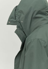 Green waterproof jacket with a high collar and interior hood; smooth texture; features snap buttons and a full-length zipper.