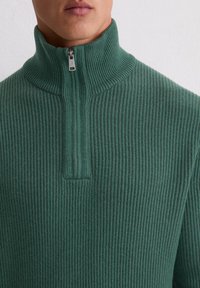 Pull en rib à col montant et fermeture éclair sur le devant. Tissu texturé avec des lignes verticales, offrant un ajustement confortable autour du cou.